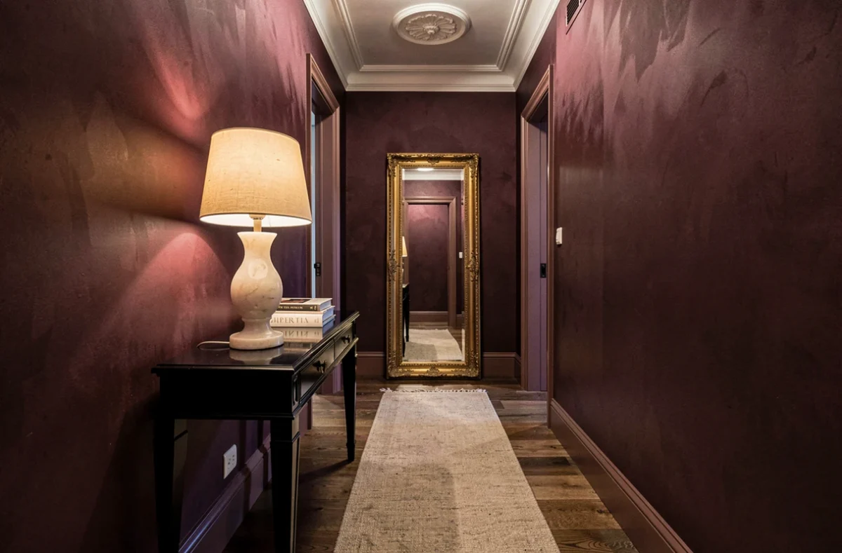 Couloir d'entrée élégant avec murs aubergine effet soie, console laquée noire, lampe en albâtre et parquet noyer pour un intérieur maison de maître