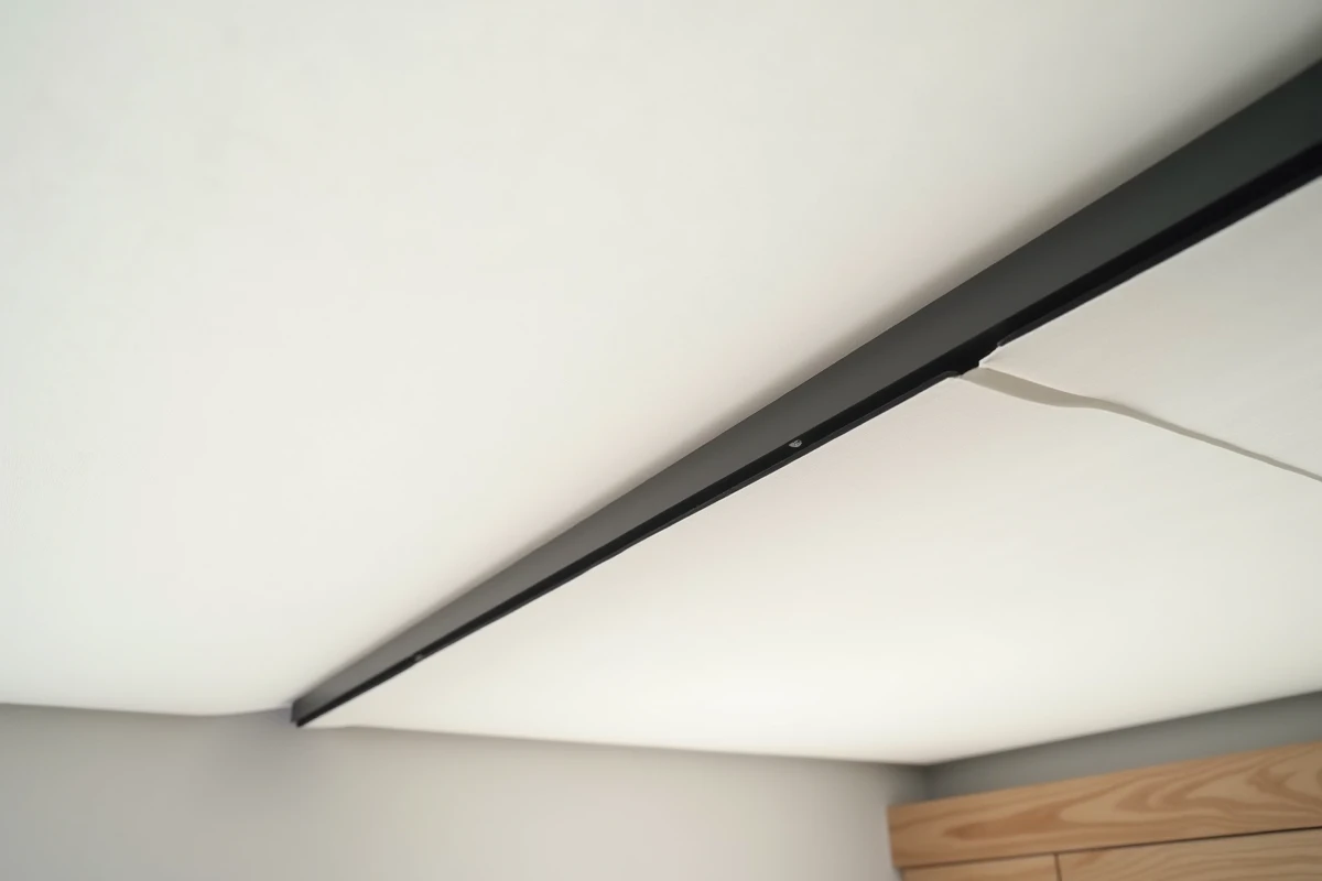 Détail de finition d'un plafond en toile tendue avec rail aluminium noir dans une chambre moderne