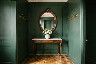 Entrée chic avec murs vert forêt mat, parquet en chevrons, console en noyer et miroir ovale en bronze doré pour un effet maison de maître